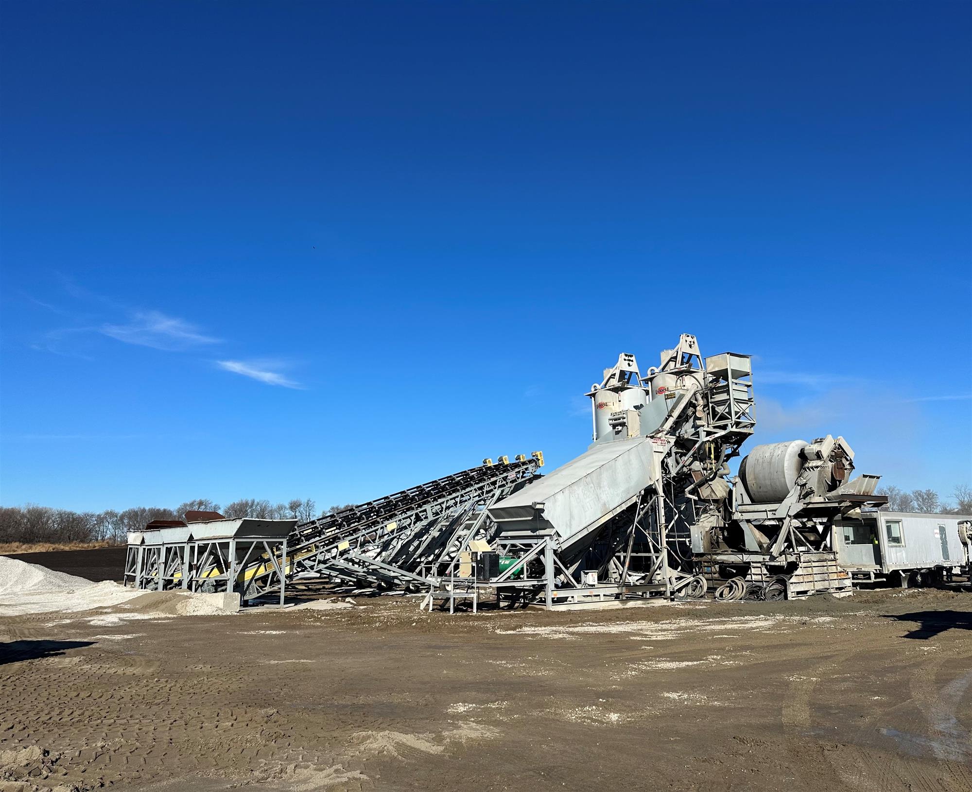 blue sky, dirt yard, metal truss conveyors, cement silos, concrete mixer